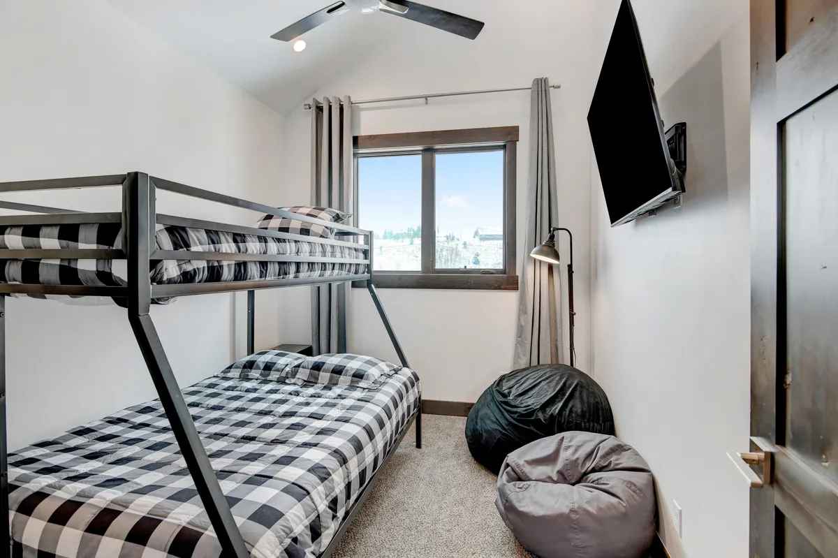 A playful bunk room with a sturdy bunk bed, cozy bean bags, and a window offering natural light. The space is thoughtfully arranged to accommodate children or groups, providing both comfort and flexibility.
