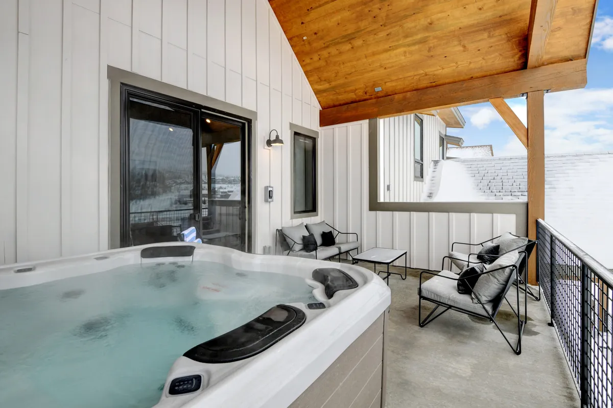 An inviting exterior view of a covered patio featuring a hot tub, modern outdoor furniture, and a wooden ceiling. Guests are seen relaxing and socializing, highlighting the patio as an all-season gathering space.