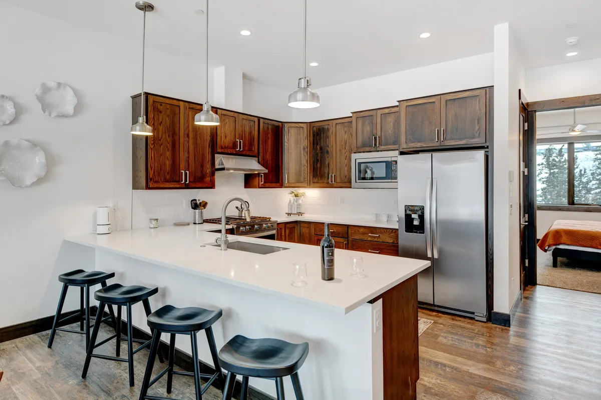 A modern, fully equipped gourmet kitchen with an island countertop, stainless steel appliances, wood cabinetry, and bar stools. The space feels inviting and ready for anything from casual breakfasts to festive dinner parties.