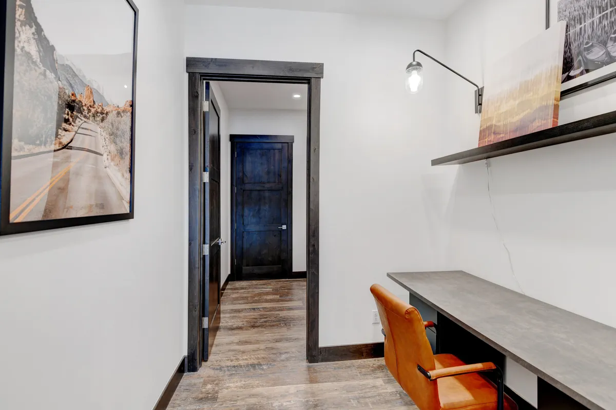 The image presents a minimalist workspace with a stylish orange chair, a sleek desk, and a framed photograph of a winding road. The setup is creative and focused, ideal for productivity, with subtle artistic elements that inspire long work sessions.