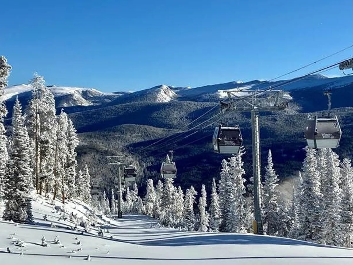 An exhilarating view of gondola lifts ascending snow-covered slopes, surrounded by snowy trees and a dramatic mountain range. The scene pulses with winter excitement and showcases the proximity to world-class skiing and snowboarding at Winter Park Resort.