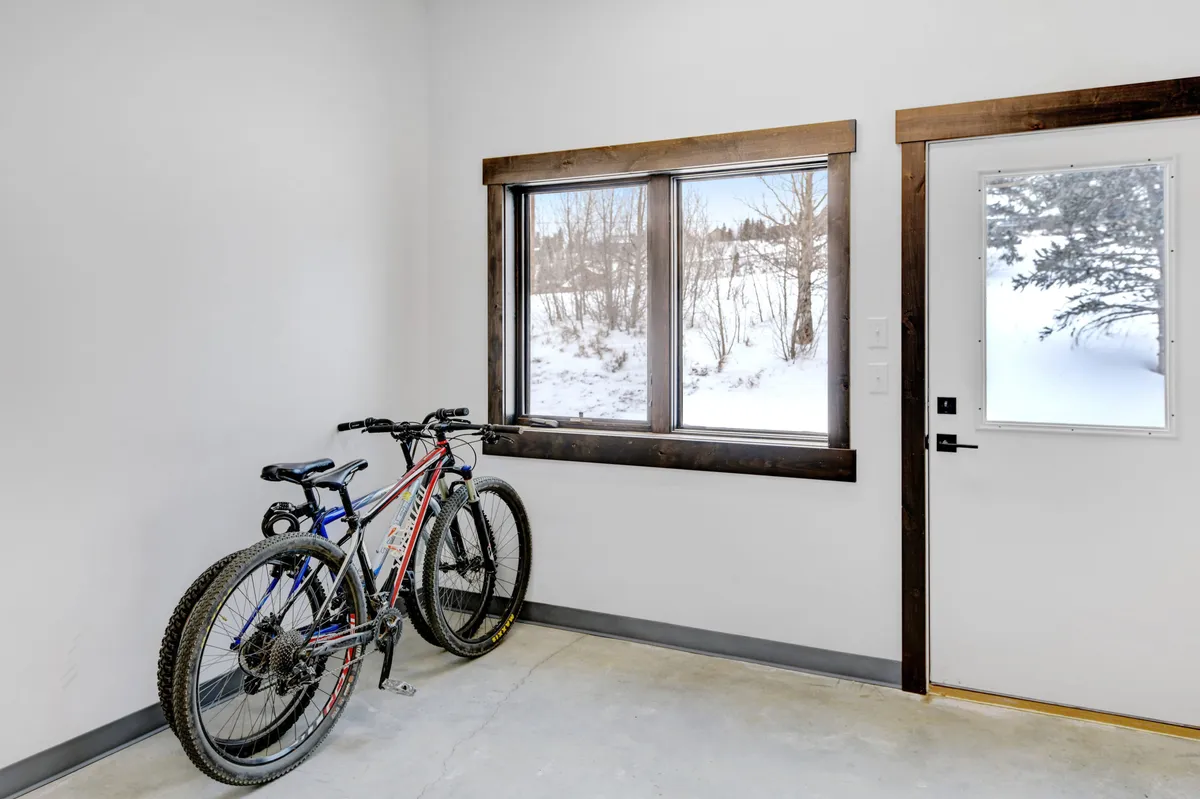 This image features two mountain bikes positioned near a large window with a snowy mountain view. The white walls and wooden trim frame the view, giving a sense of the outdoors and adventure, while the bikes nod to active pursuits in the Rockies.