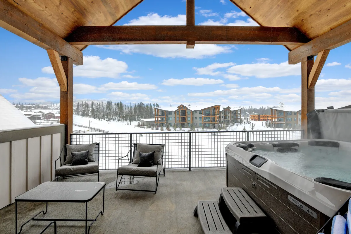 This exterior shot showcases a bubbling hot tub set amidst chic outdoor seating, with a panoramic view of the mountains in the background. The scene is tranquil and inviting, depicting people enjoying the hot tub and relaxing outdoors.
